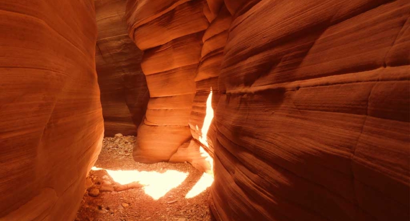 The sun shines through into a red slot canyon